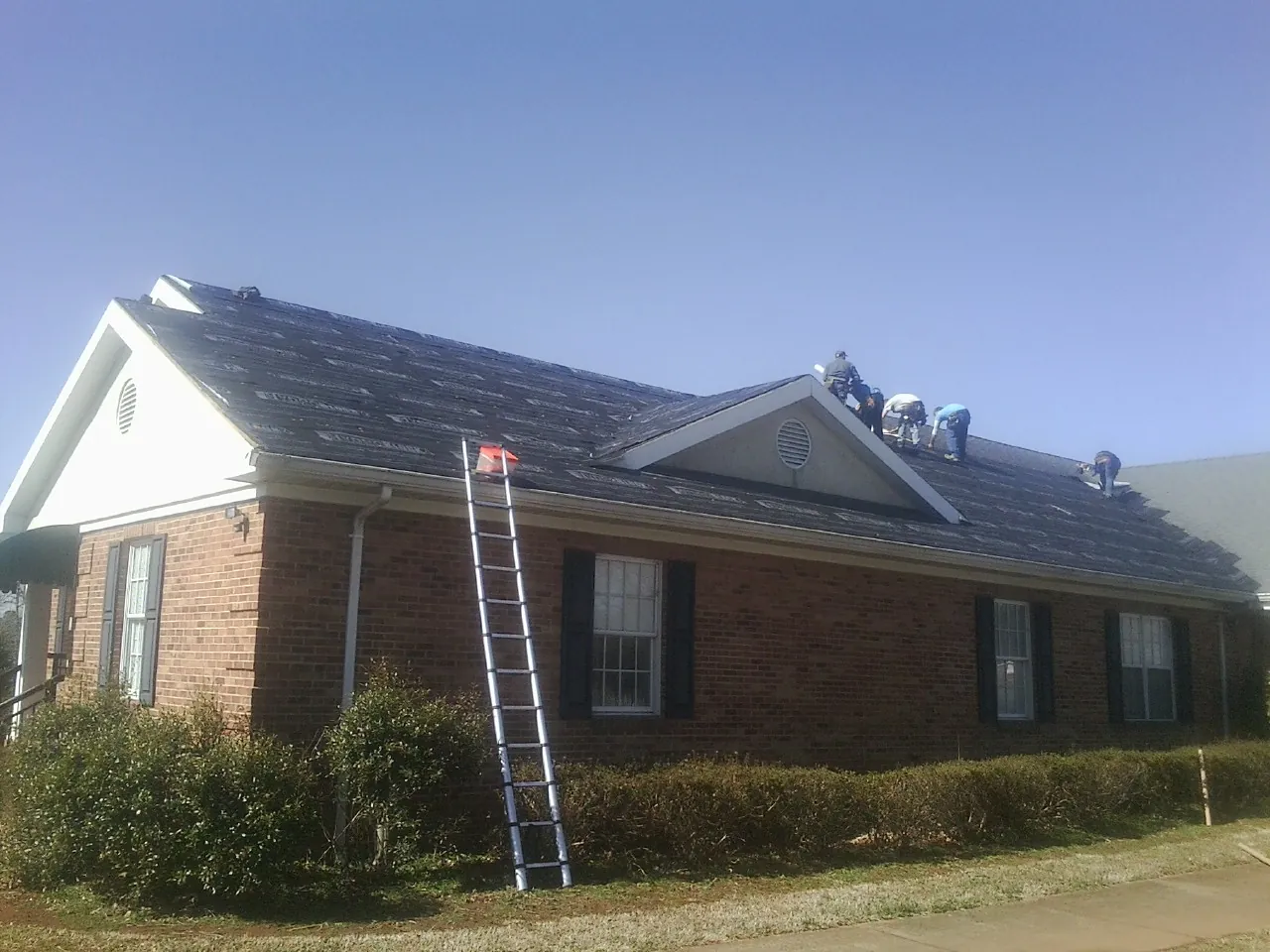 Crew tearing shingles off a brick ranch roof with a ladder set — Metal Roof Repair work by our crew in Green Cove Springs
