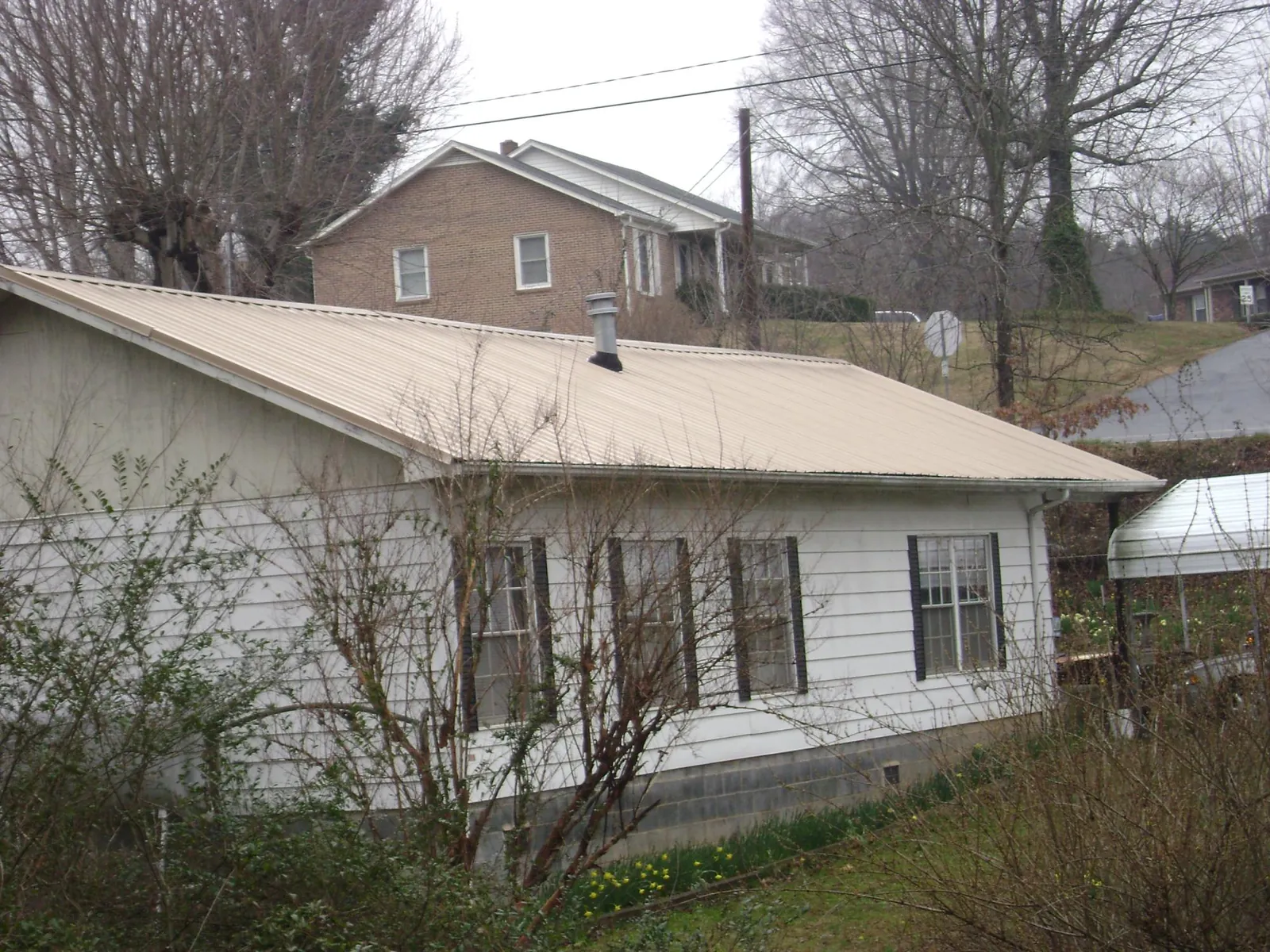Tan metal roof on a white sided house set into a hillside — Commercial Roofing by Roofing Brothers in Green Cove Springs